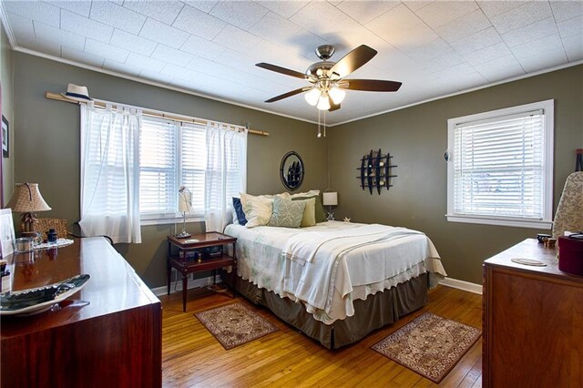 bedroom with ornamental molding, ceiling fan, baseboards, and hardwood / wood-style floors