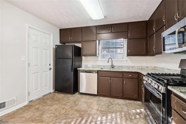 kitchen with appliances with stainless steel finishes, dark brown cabinetry, light stone counters, and sink