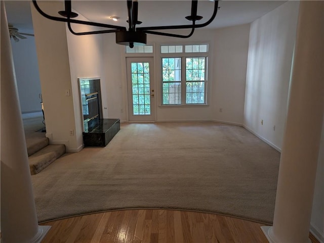 unfurnished living room featuring a high end fireplace, light wood-type flooring, ornate columns, and ceiling fan