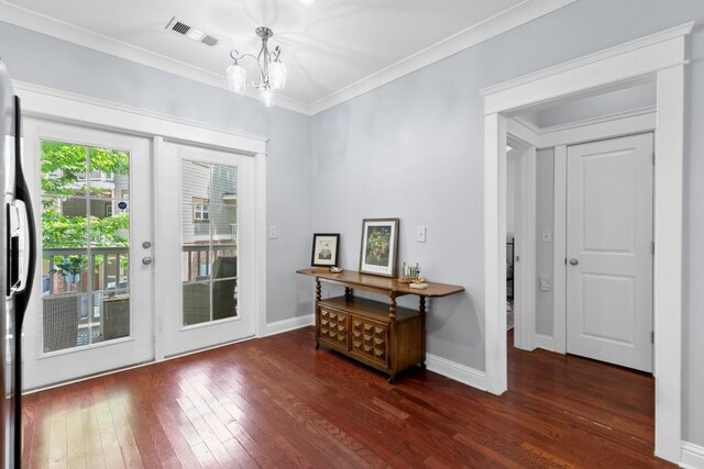 doorway with an inviting chandelier, wood-type flooring, baseboards, visible vents, and ornamental molding