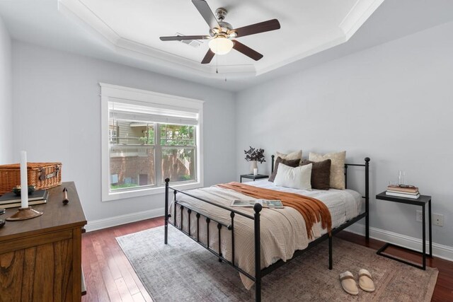 bedroom with baseboards, a tray ceiling, ornamental molding, and wood finished floors