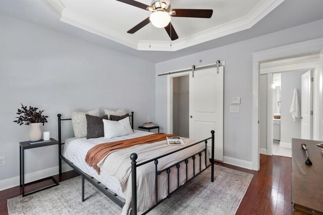 bedroom featuring a barn door, wood-type flooring, baseboards, a tray ceiling, and a closet