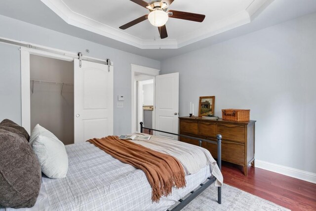 bedroom featuring a barn door, wood finished floors, baseboards, a closet, and a tray ceiling
