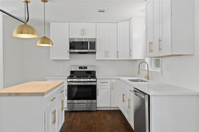 kitchen with stainless steel appliances, a sink, white cabinets, hanging light fixtures, and light countertops