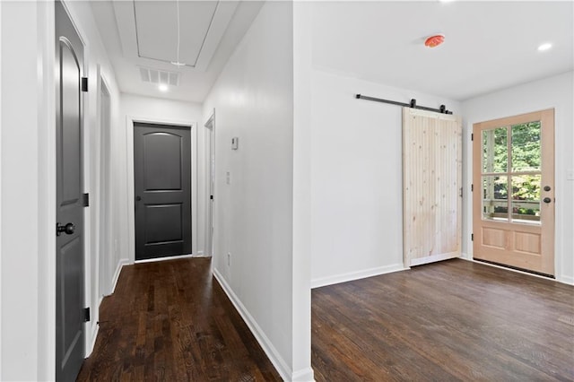 interior space with dark wood-style floors, visible vents, a barn door, attic access, and baseboards