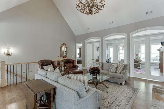 living room featuring wood finished floors, visible vents, french doors, high vaulted ceiling, and a notable chandelier
