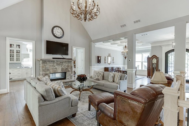 living area featuring a stone fireplace, visible vents, high vaulted ceiling, and an inviting chandelier