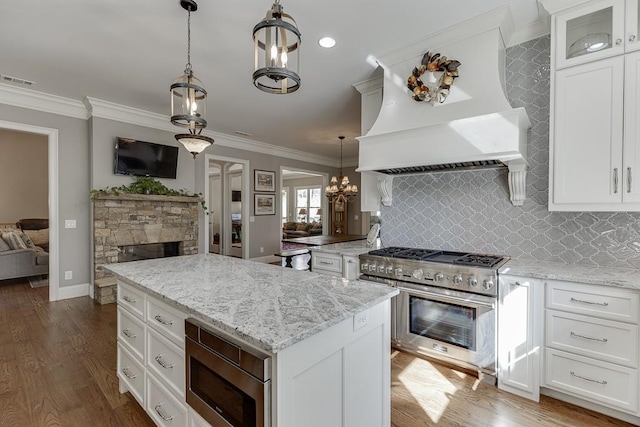 kitchen featuring crown molding, custom exhaust hood, stainless steel appliances, light stone countertops, and a kitchen island