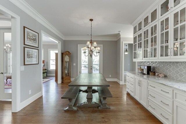 dining space featuring french doors, dark wood finished floors, baseboards, a chandelier, and ornamental molding