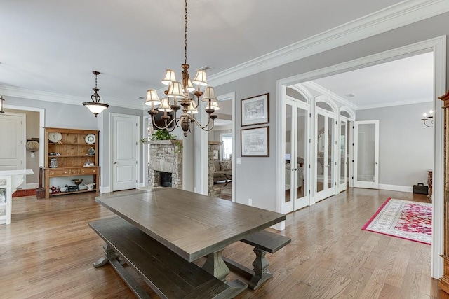 dining area featuring a stone fireplace, ornamental molding, baseboards, light wood-style flooring, and a notable chandelier