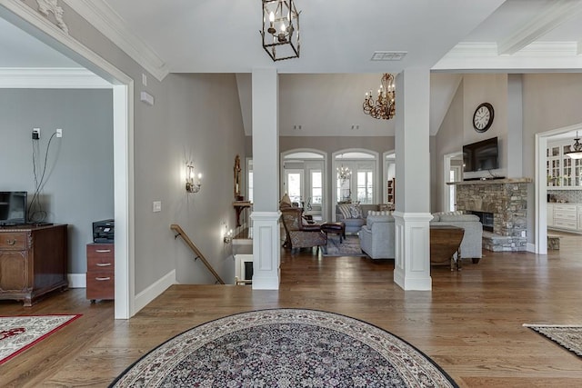 entrance foyer featuring ornate columns, wood finished floors, visible vents, a fireplace, and a notable chandelier