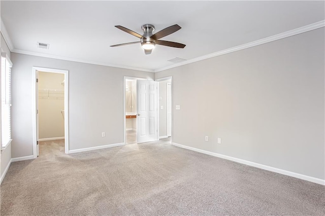 unfurnished bedroom featuring light carpet, a walk in closet, ceiling fan, ornamental molding, and a closet