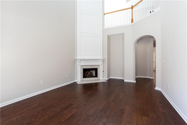 unfurnished living room featuring a high end fireplace, dark hardwood / wood-style floors, and a high ceiling