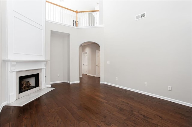 unfurnished living room with a fireplace, a high ceiling, and dark hardwood / wood-style floors