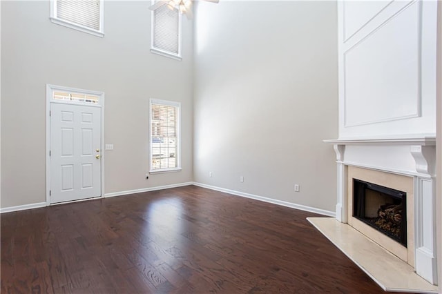 unfurnished living room with ceiling fan, dark hardwood / wood-style flooring, and a high ceiling