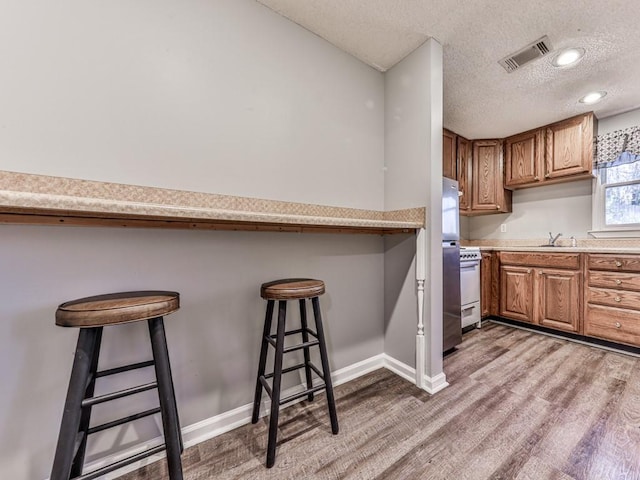 5090 Eubanks Rd, Woodstock, GA 30188 - kitchen with wood finished floors, brown cabinetry, a kitchen breakfast bar, a textured ceiling, and light countertops