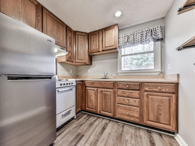 5090 Eubanks Rd, Woodstock, GA 30188 - kitchen featuring freestanding refrigerator, gas range gas stove, light wood-style floors, brown cabinets, and a textured ceiling