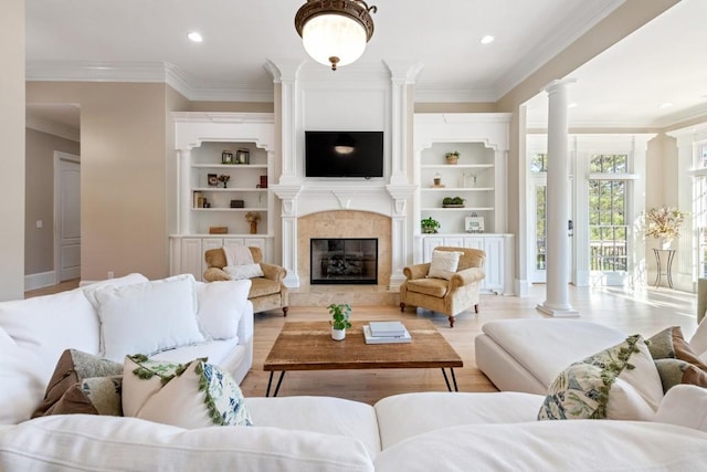 living area with light wood-style flooring, built in features, crown molding, a premium fireplace, and ornate columns