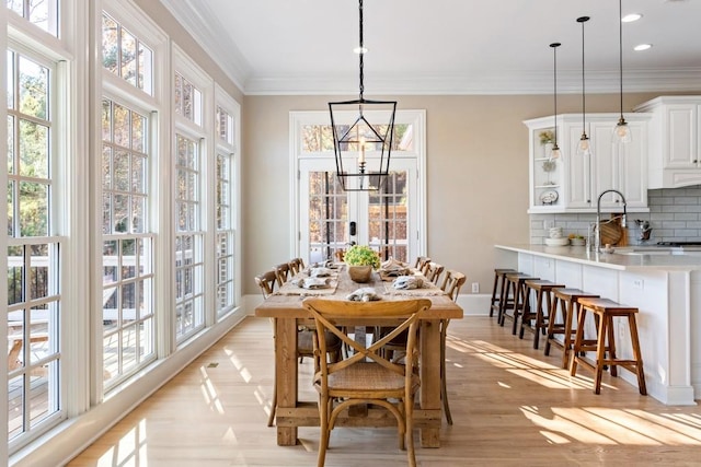 dining space featuring a notable chandelier, sink, light wood-type flooring, and ornamental molding