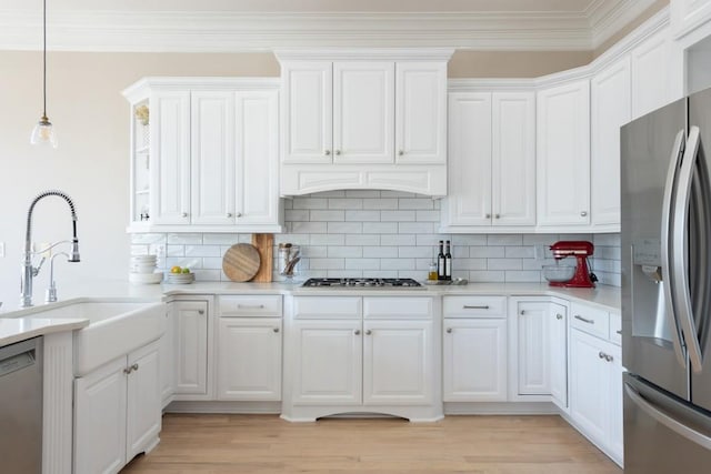 kitchen with crown molding, light countertops, appliances with stainless steel finishes, white cabinets, and a sink