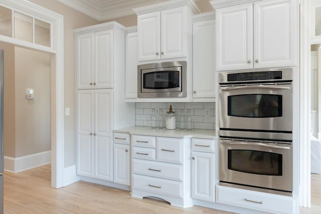 kitchen with white cabinets, crown molding, decorative backsplash, light wood-type flooring, and appliances with stainless steel finishes