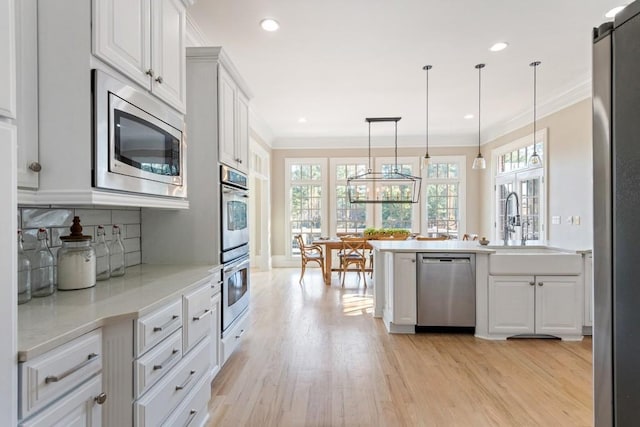 kitchen with crown molding, a wealth of natural light, light wood-style floors, and appliances with stainless steel finishes