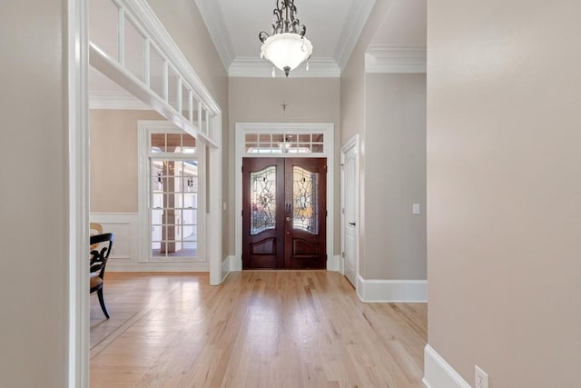 entryway with baseboards, light wood-style flooring, ornamental molding, french doors, and wainscoting