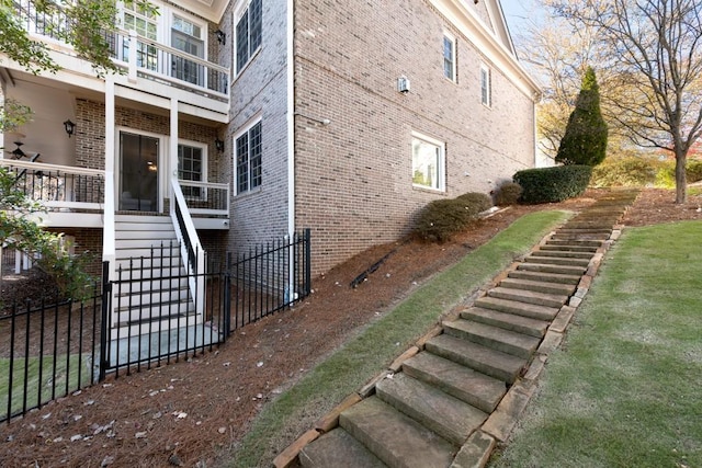 view of home's exterior featuring a balcony, stairway, fence, and brick siding