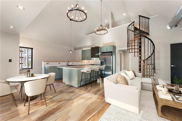 living room featuring sink, a notable chandelier, high vaulted ceiling, and light wood-type flooring