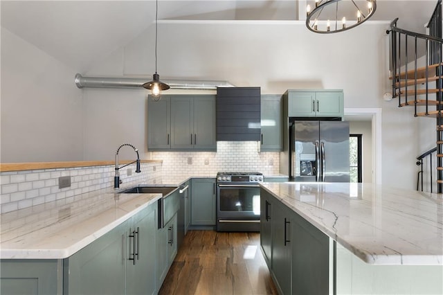 kitchen with sink, wall chimney range hood, appliances with stainless steel finishes, hanging light fixtures, and light stone countertops