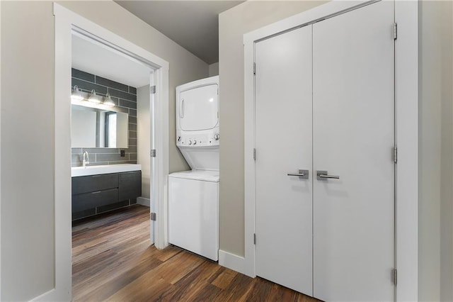 laundry room with sink, dark wood-type flooring, and stacked washing maching and dryer