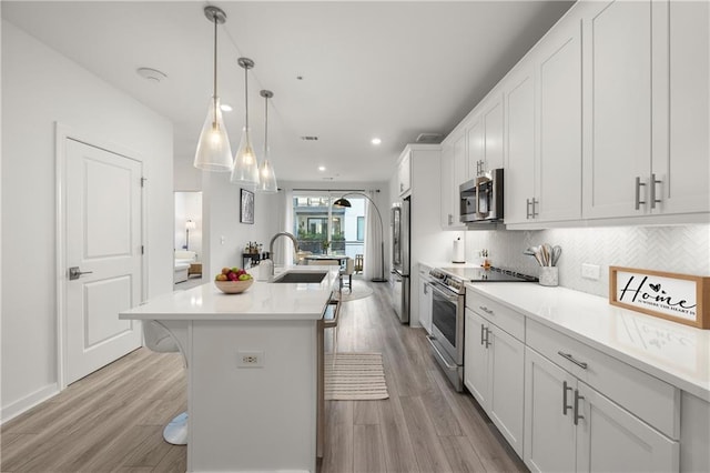 kitchen featuring a kitchen bar, white cabinetry, stainless steel appliances, sink, and a kitchen island with sink