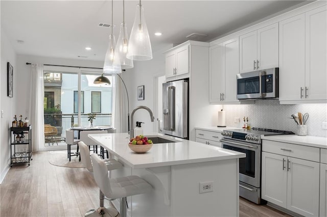 kitchen with visible vents, light countertops, decorative backsplash, appliances with stainless steel finishes, and a kitchen island with sink