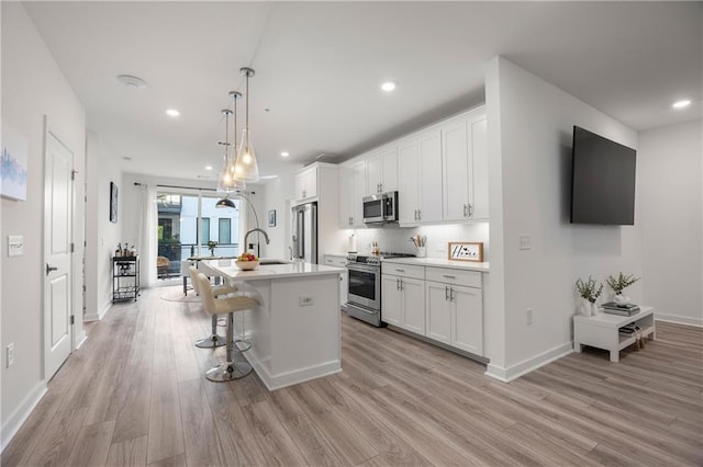 kitchen featuring white cabinets, stainless steel appliances, light wood-style flooring, and a kitchen island with sink