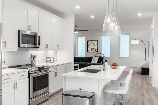 kitchen featuring an island with sink, light wood-style flooring, a sink, tasteful backsplash, and stainless steel appliances