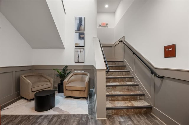 stairs with wood finished floors, wainscoting, and a decorative wall