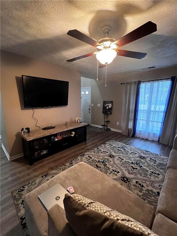 living room with ceiling fan, a textured ceiling, and dark hardwood / wood-style flooring