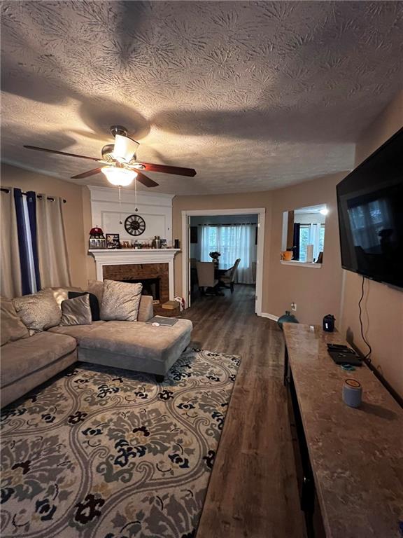 living room with a textured ceiling, ceiling fan, and dark wood-type flooring