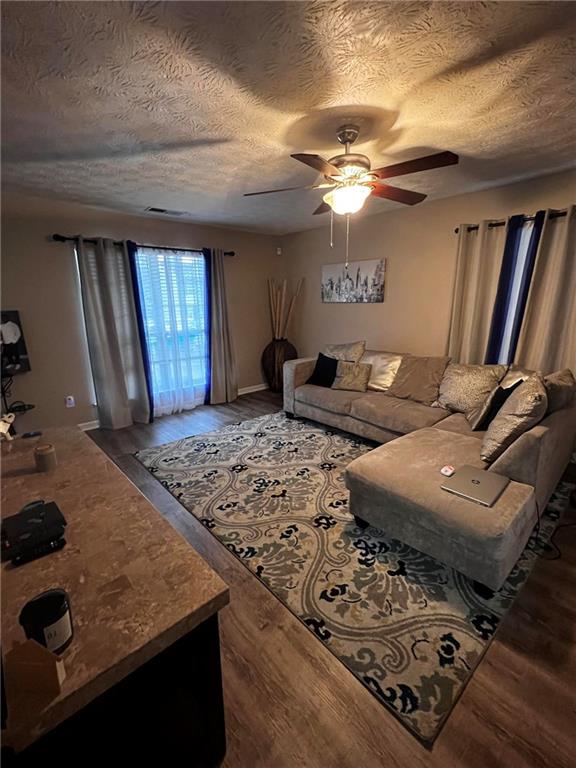 living room featuring ceiling fan, a textured ceiling, and wood-type flooring