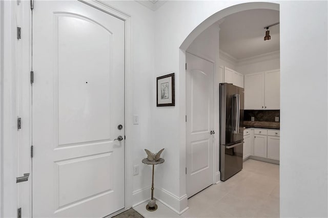 entryway featuring baseboards, ornamental molding, track lighting, light tile patterned floors, and arched walkways