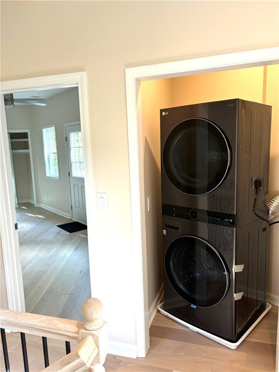 washroom featuring stacked washing maching and dryer, ceiling fan, and light wood-type flooring