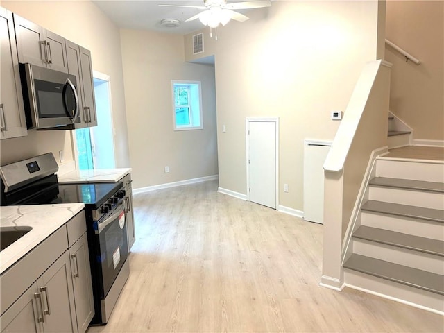 kitchen with light hardwood / wood-style flooring, gray cabinets, ceiling fan, appliances with stainless steel finishes, and light stone countertops