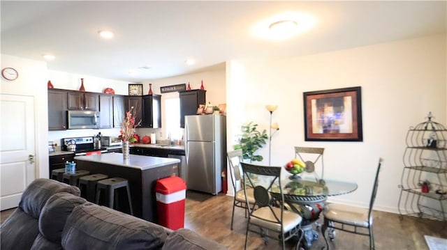 kitchen with appliances with stainless steel finishes, wood-type flooring, a breakfast bar, a center island with sink, and dark brown cabinets