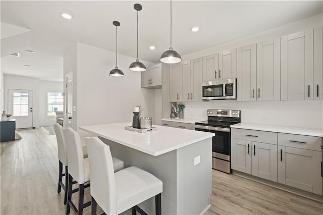 kitchen featuring stainless steel appliances, hanging light fixtures, gray cabinetry, light hardwood / wood-style flooring, and a center island