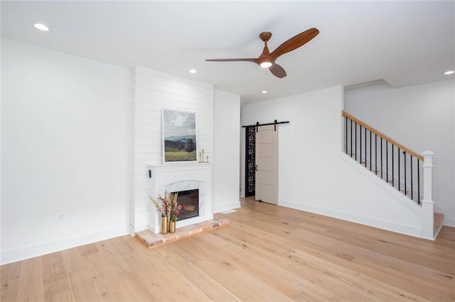 unfurnished living room featuring ceiling fan, a barn door, a fireplace, and light wood-type flooring