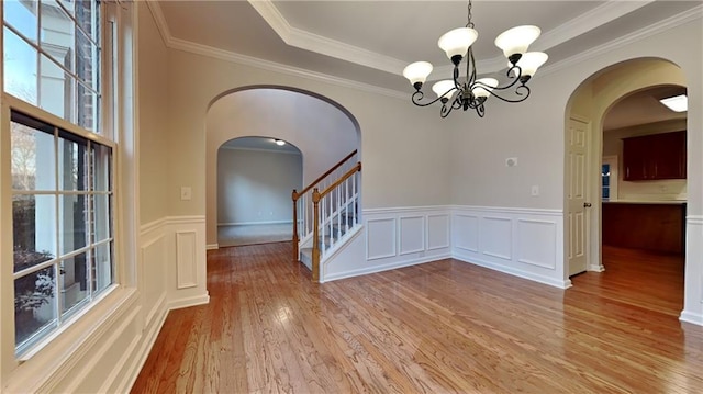 unfurnished dining area featuring a raised ceiling, crown molding, an inviting chandelier, and light wood-type flooring