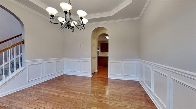 spare room featuring a tray ceiling, crown molding, a chandelier, and light wood-type flooring