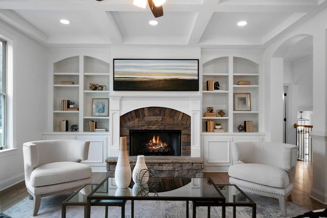 living area featuring coffered ceiling, hardwood / wood-style floors, a stone fireplace, and beam ceiling