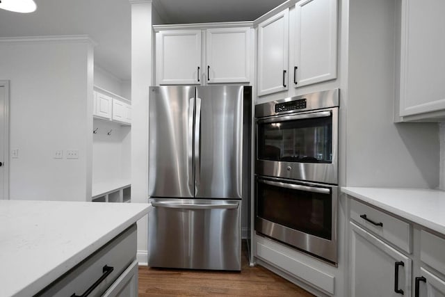 kitchen with crown molding, appliances with stainless steel finishes, white cabinets, and dark hardwood / wood-style flooring