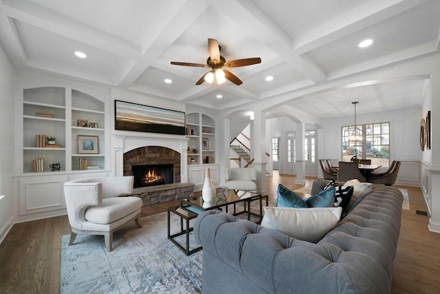 living room featuring coffered ceiling, a stone fireplace, wood-type flooring, and beamed ceiling